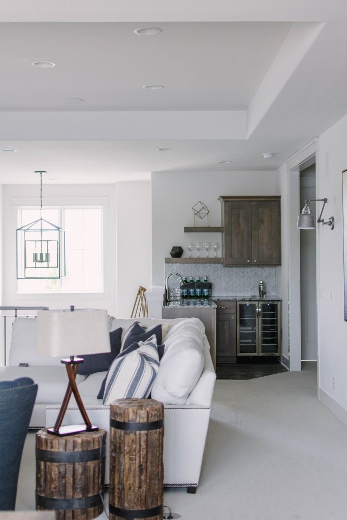 Neutral loft living room with white sectional, herringbone backsplash, wood cabinets and blue and green accents. Omaha Street of Dreams design by Pearson & Company. Image via Mandy McGregor Photography.