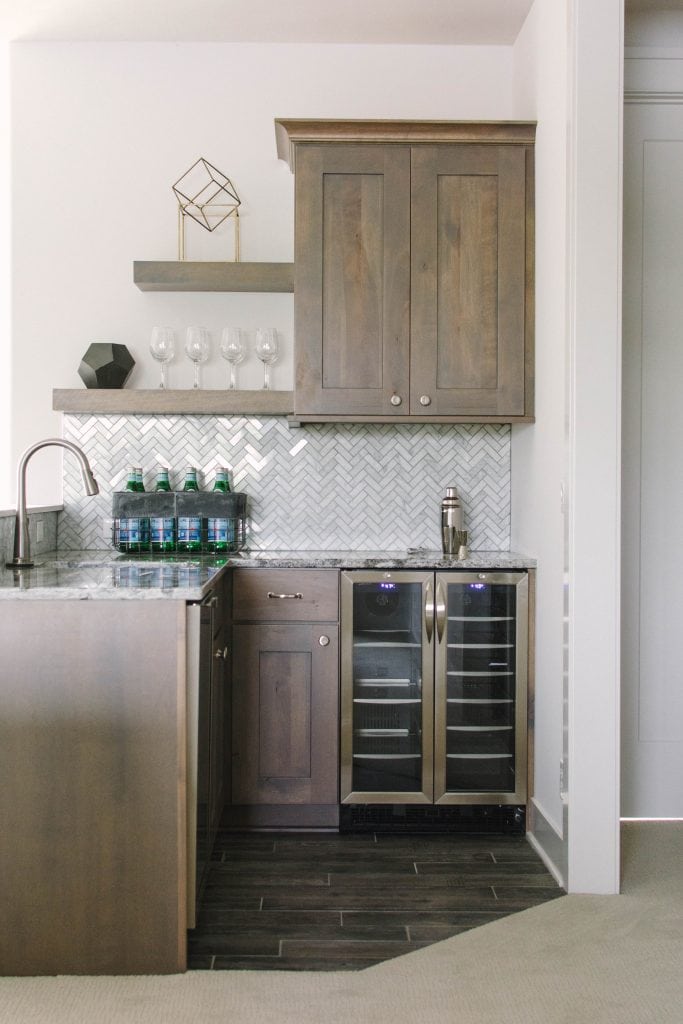 Neutral loft living room with white sectional, herringbone backsplash, wood cabinets and blue and green accents. Omaha Street of Dreams design by Pearson & Company. Image via Mandy McGregor Photography.