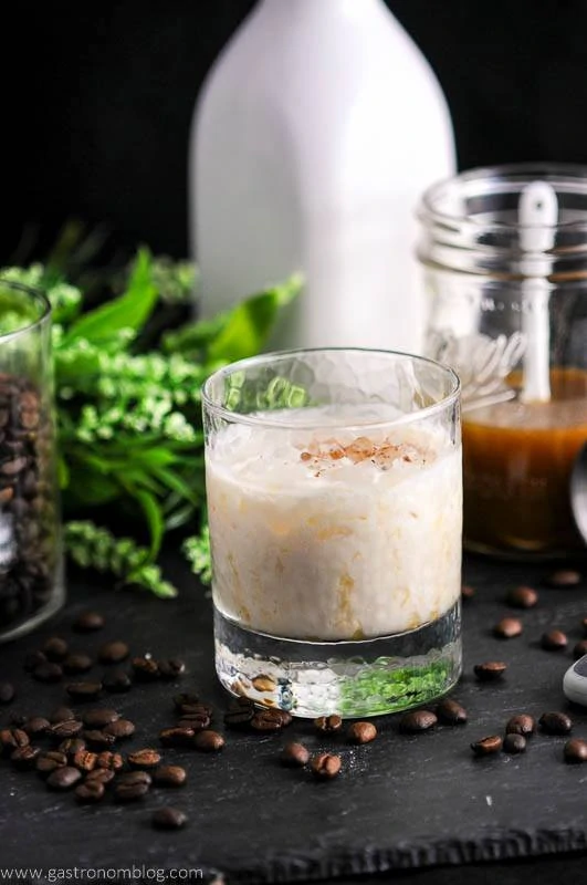 Clear glass with white boozy drink inside on a counter with coffee beans beside it.