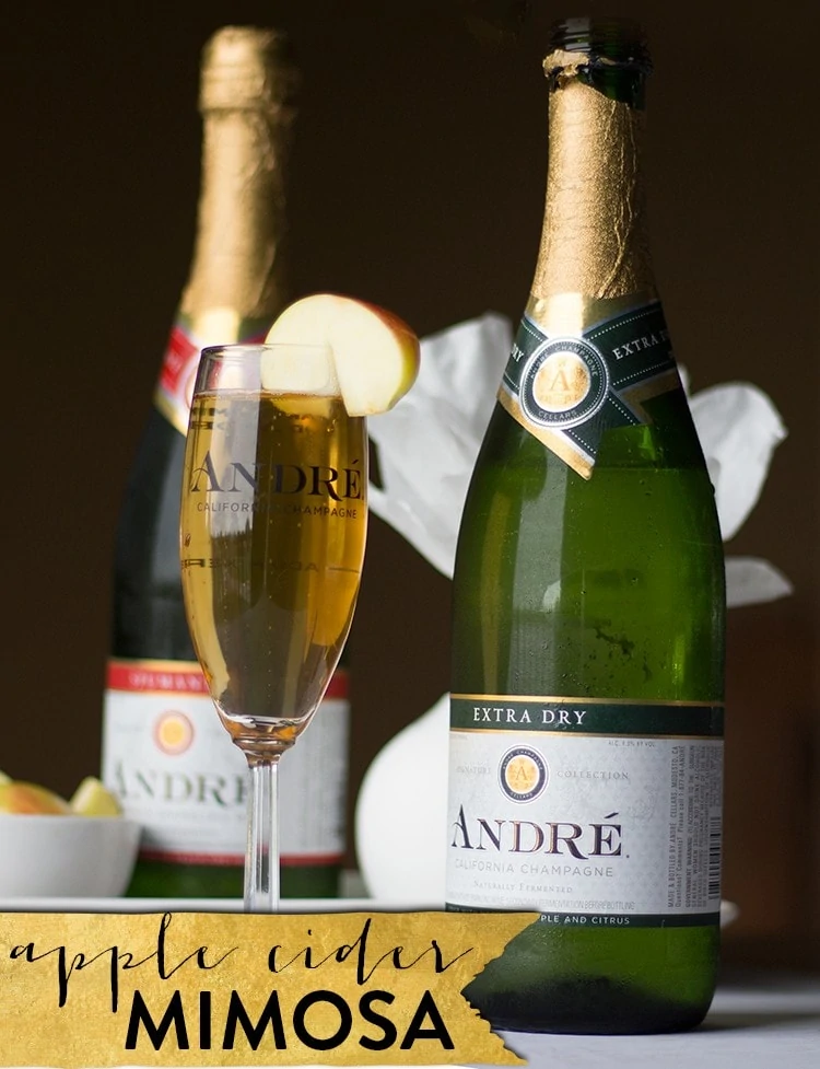 Apple cider mimosa in a champagne glass with champagne bottles behind it.