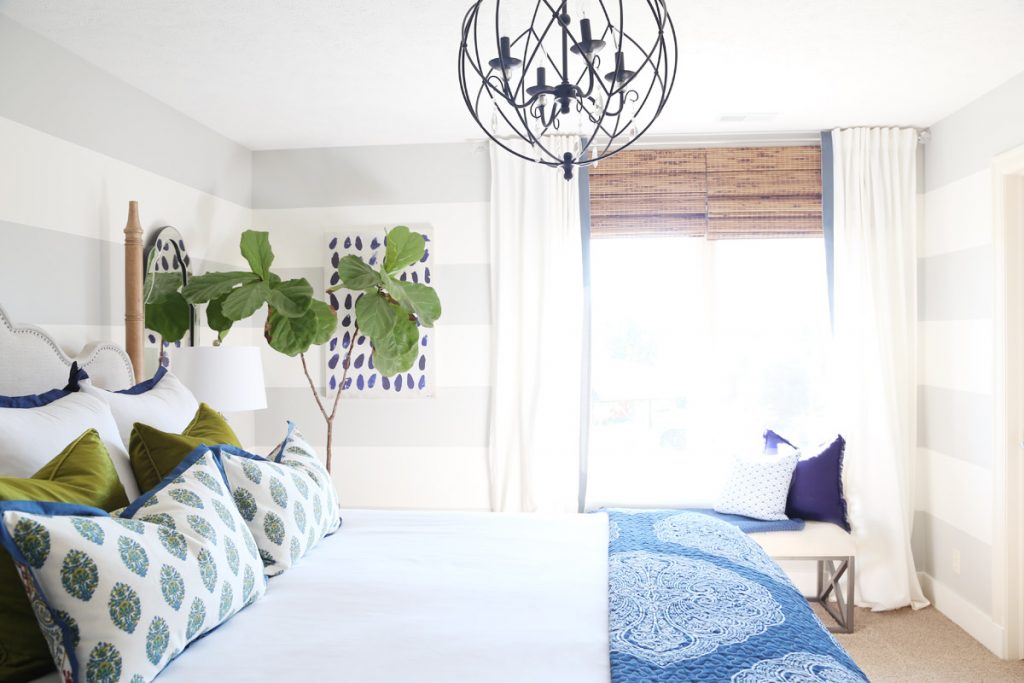 Soft blue and green bedroom with black chandelier above bed.