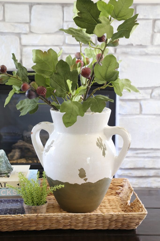 White and green vase filled with branches of leaves and berries.