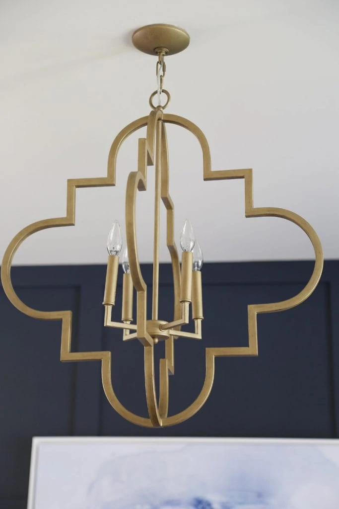A brushed gold pendant light hanging in the office in front of a navy blue wall.