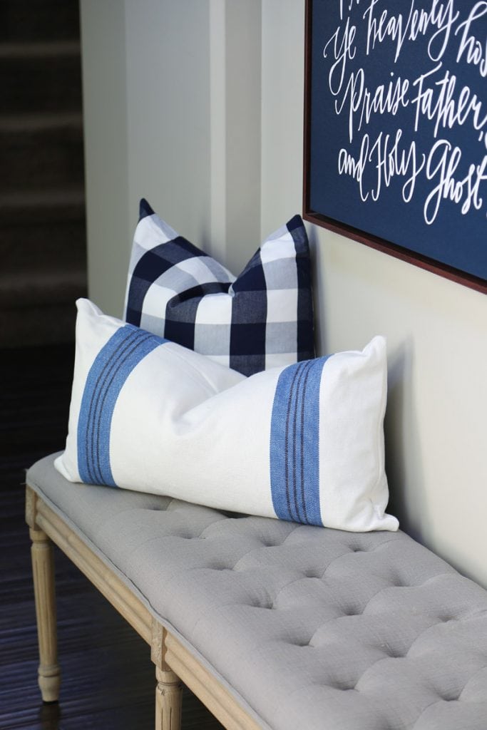 Blue and white striped, checkered pillows on a gray tufted bench.