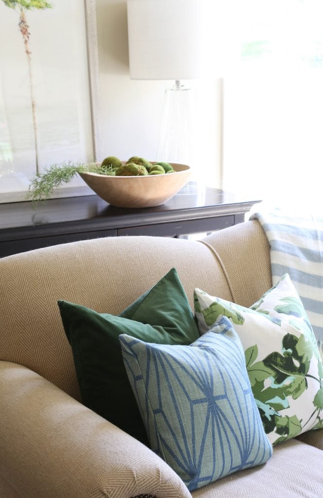 Green, blue pillows on beige couch with a wooden bowl in the background.