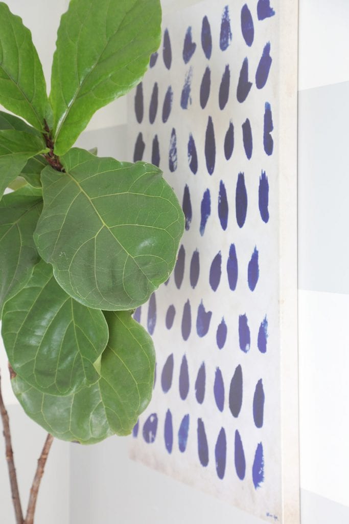 Large green plant in bedroom with blue and white art on wall.