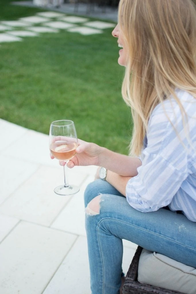 Blonde woman holding a glass of wine while sitting down.