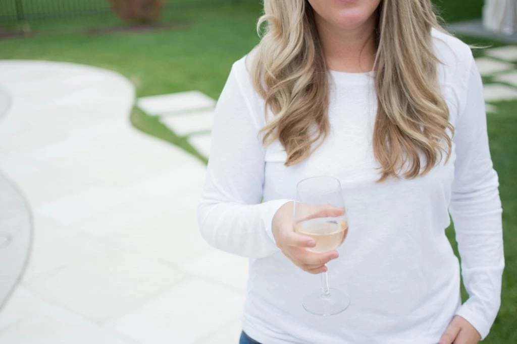 Blonde woman holding a glass of wine in the back yard.