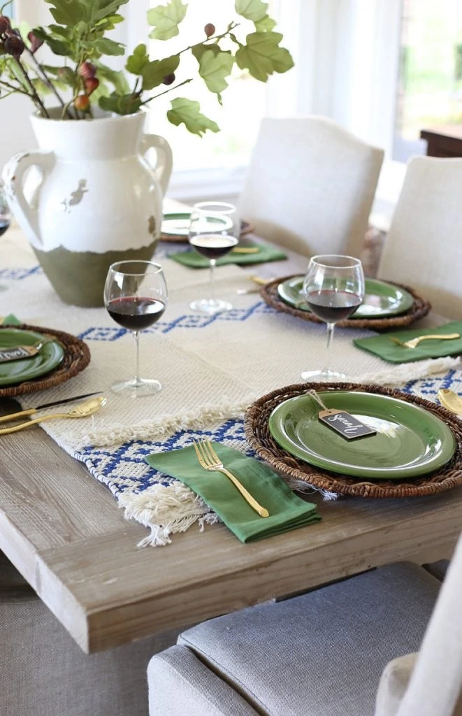 Table set for thanksgiving with green plates, and napkins and white and blue table runner.