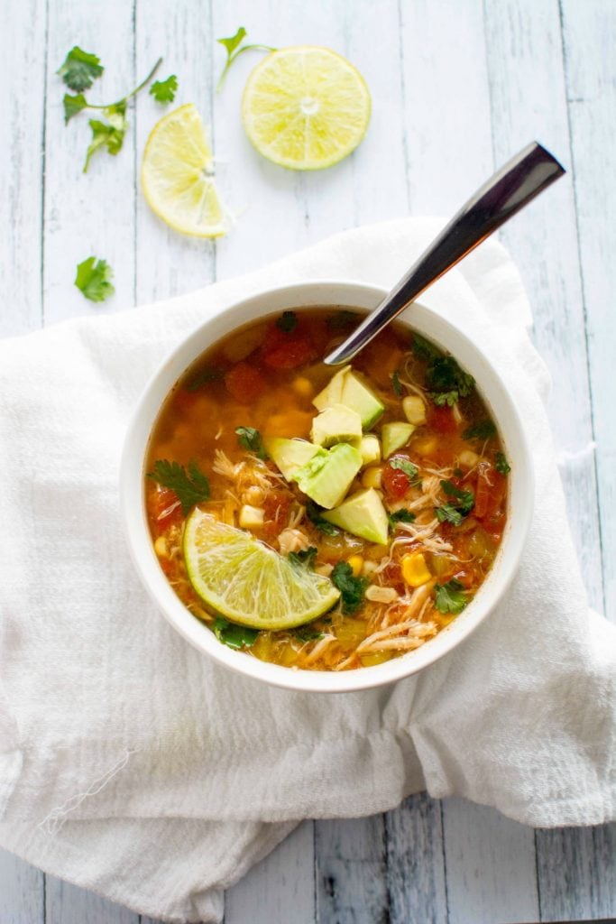 White bowl with silver spoon and soup inside with lime on top.