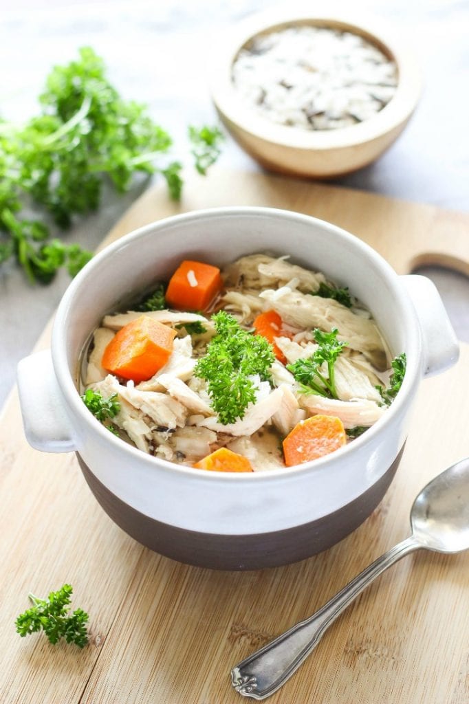 Chicken and wild rice soup in a bowl with carrots and parsley in it.