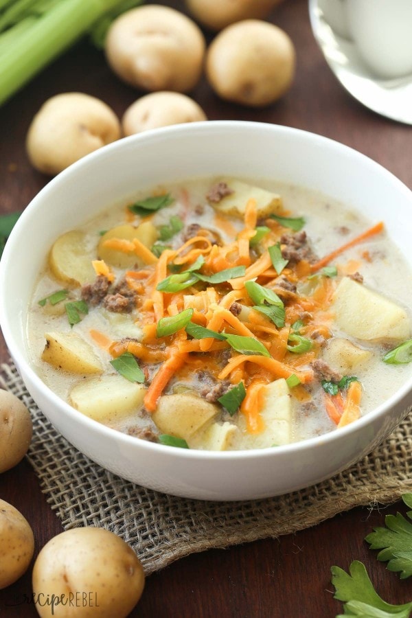 Cheeseburger stew with potatoes and cheese on top sitting on the table with potatoes around it.