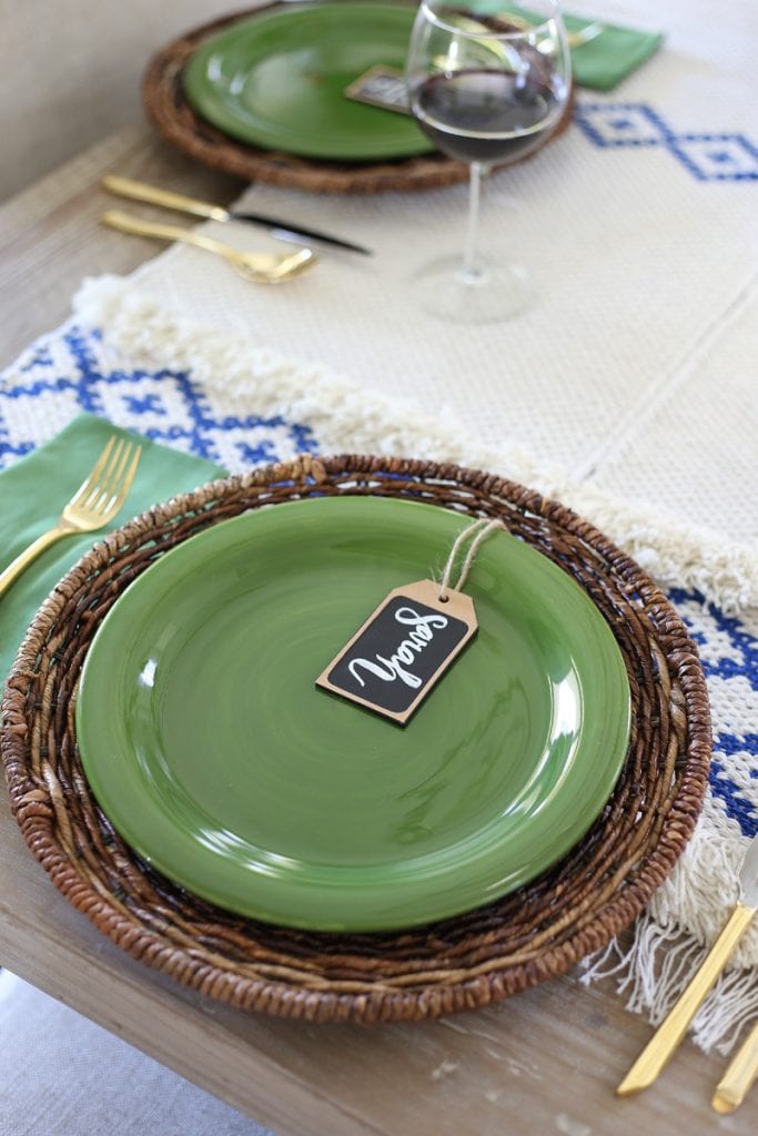 Green plates on a wicker charger with name place tags on plates.