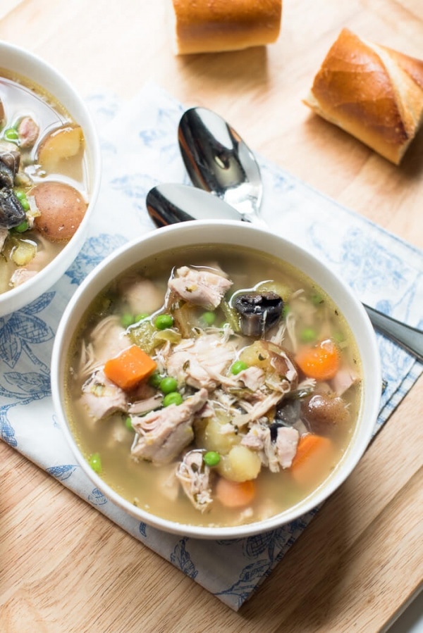 Chicken and vegetable soup on table with bread.