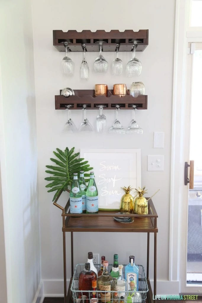 A wooden serving tray as a bar area with glasses hanging above it.