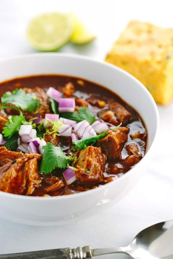 Mexican pork chili in a white bowl with a spoon beside it.