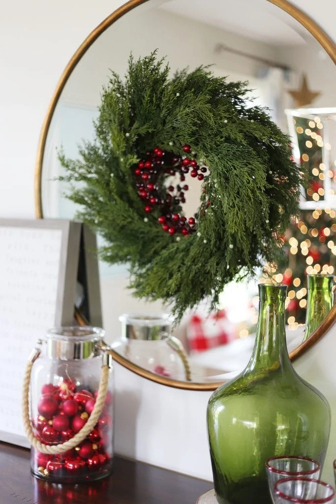 Green Christmas wreath with red berries on a gold mirror in dining room.