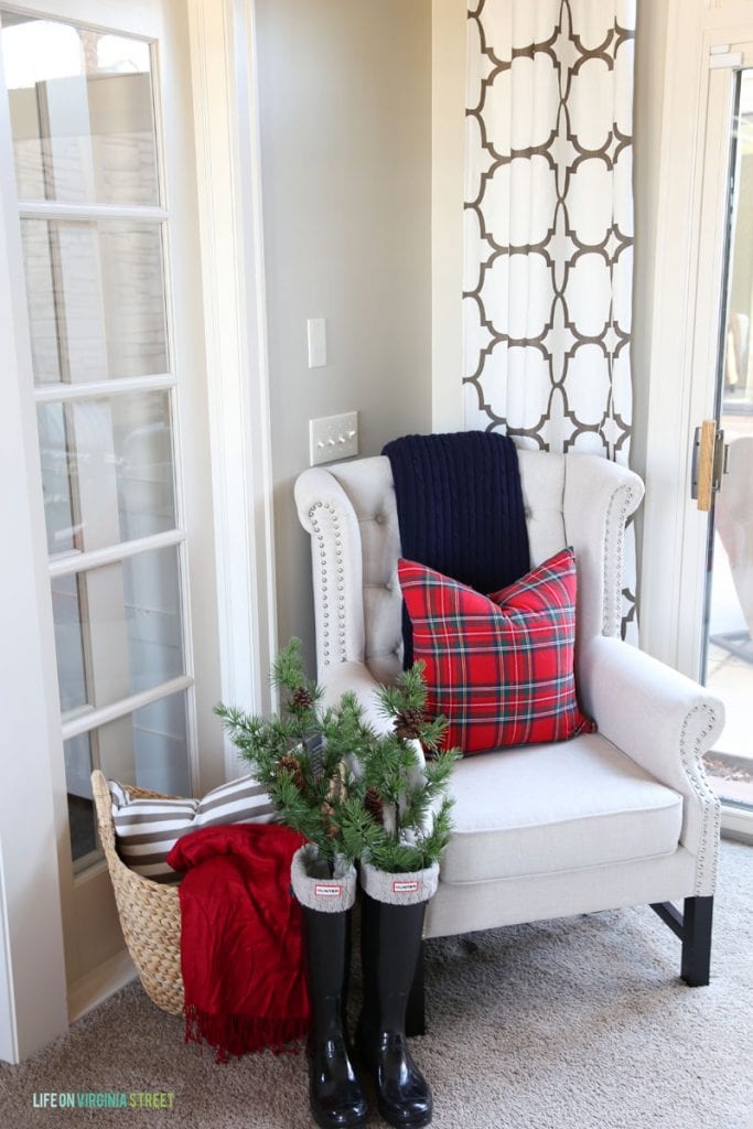 White armchair in corner of room with Hunter boots beside it and pine tree branches inside the black boots.