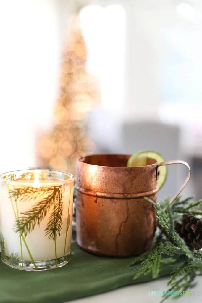 A copper mug and a clear glass with holiday drink inside on a green tablecloth.