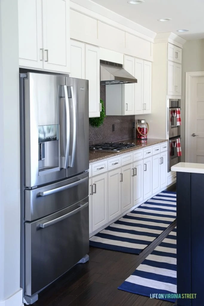 Stainless steel fridge in kitchen with striped blue and white rug on the floor.