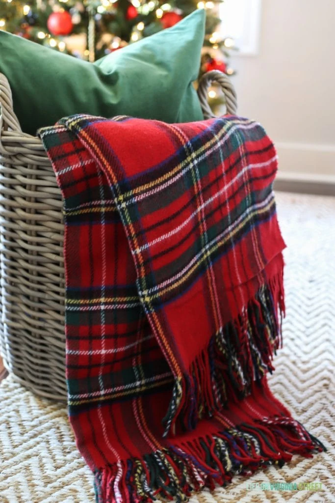 A plaid throw in a basket with a green pillow.
