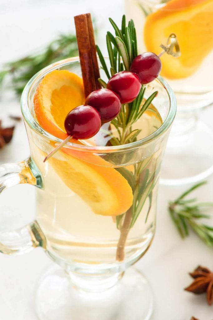Slow Cooker White Spiced Wine - Yes, you can make cocktails using your slow cooker! Like this delicious spiced wine with beautiful garnish of cranberry, orange, rosemary and a cinnamon stick.