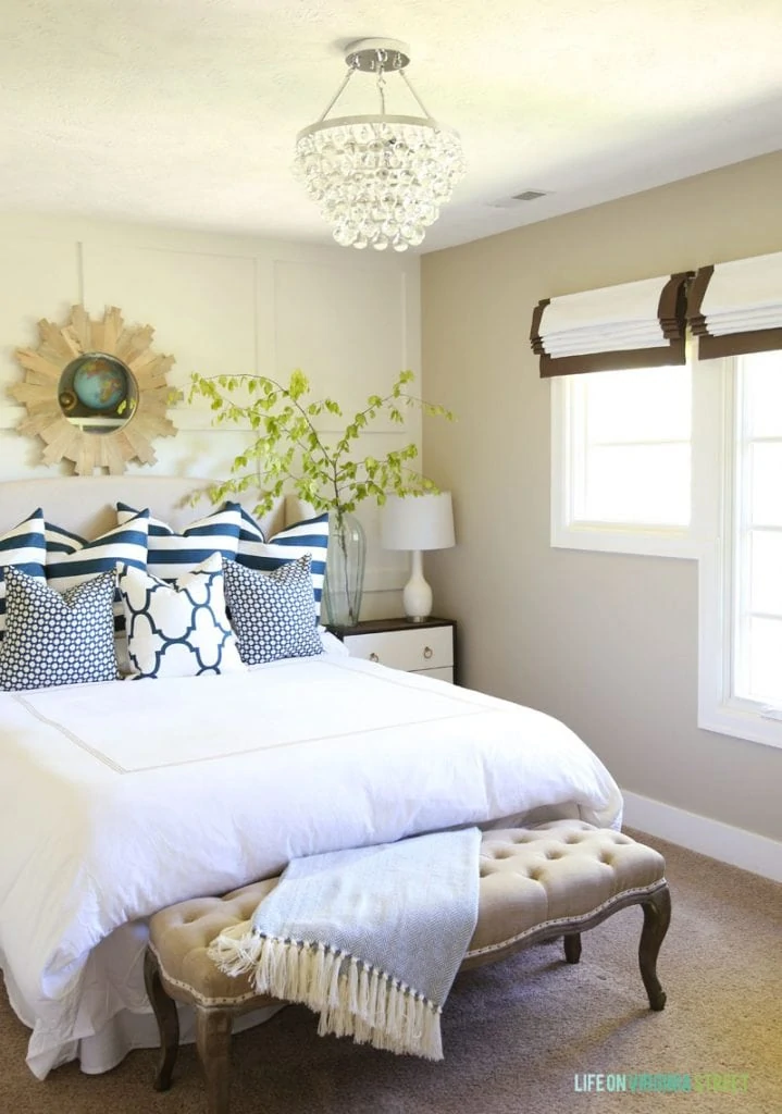 Guest bedroom with white bedding, navy blue and white pillows, and ribbon trimmed roman shades. Love the accent wall with board and batten grids behind the bed!