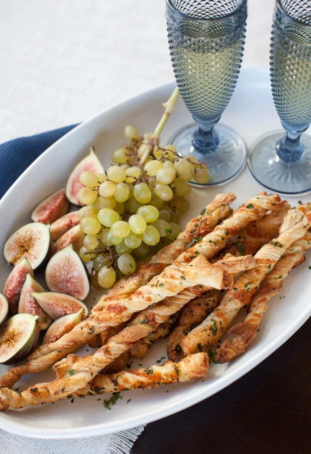 Cheese twists on a plate with grapes and figs.