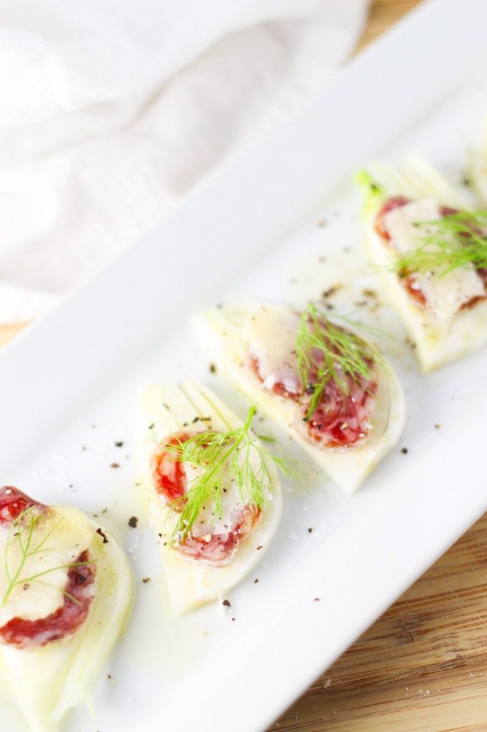 Little fennel and salami open sandwiches on a white tray.