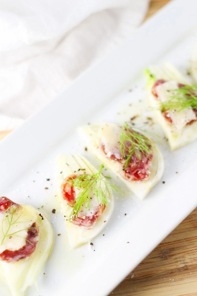 Little fennel and salami open sandwiches on a white tray.