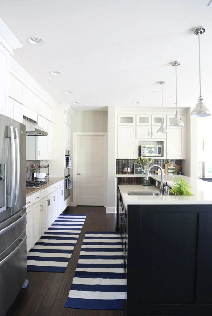 White kitchen with black island and navy blue and white striped runners.