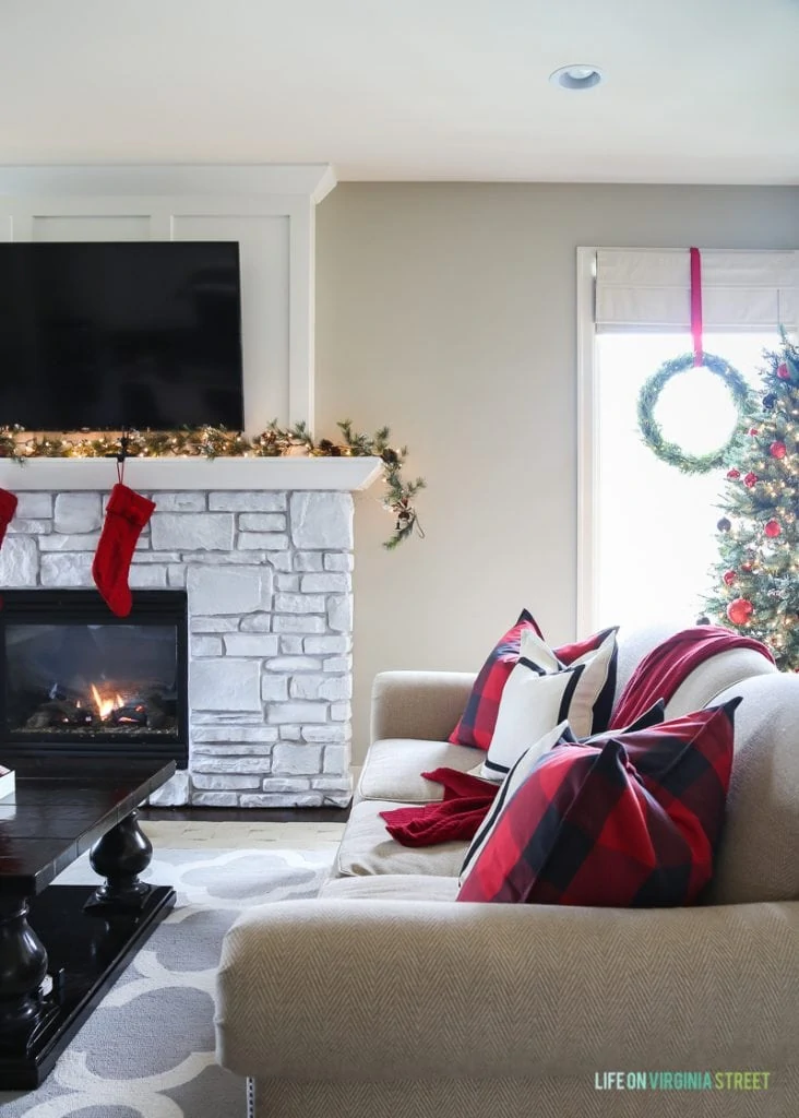 White fireplace mantel with red stocking hanging on it, and red pillows on couch.