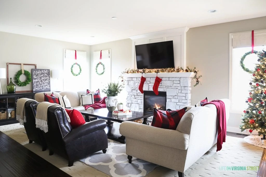 Living room with neutral couch and red pillows on couch and wreaths hanging on windows.