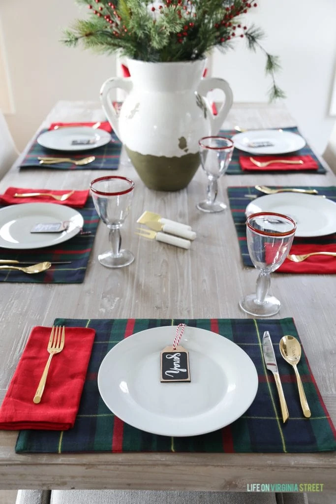 Red rimmed wine glasses on table with white plates, name tags and vase filled with greenery.