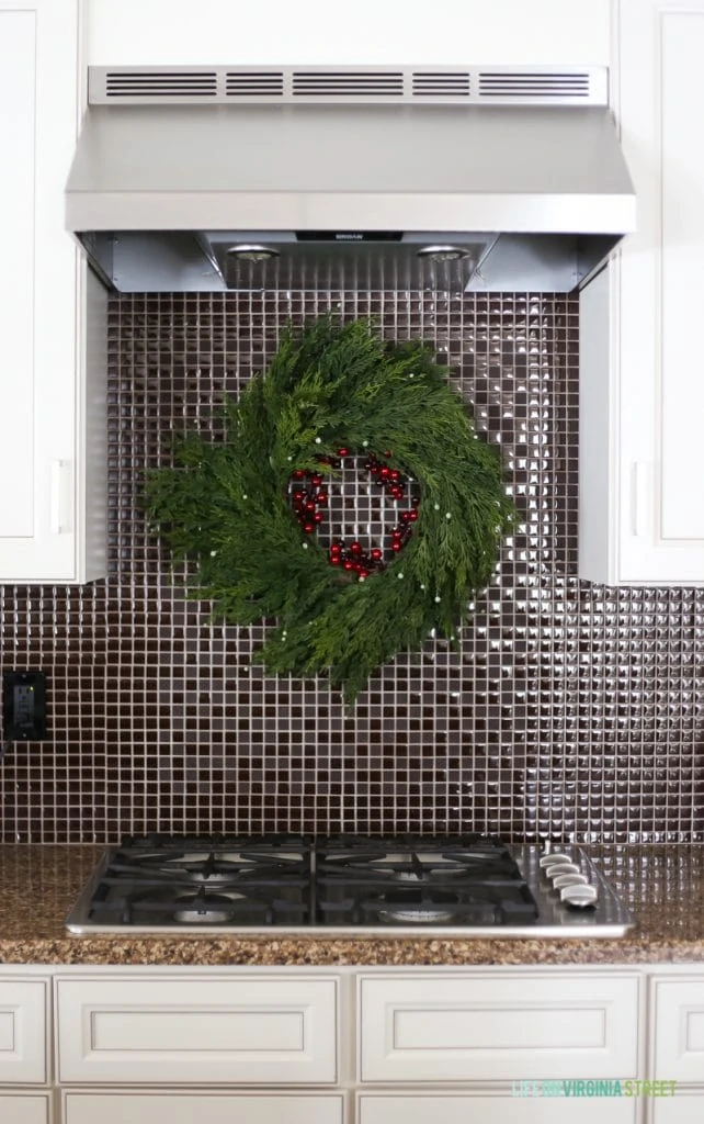 Faux cedar wreath hanging over stove on backsplash in a Christmas kitchen.