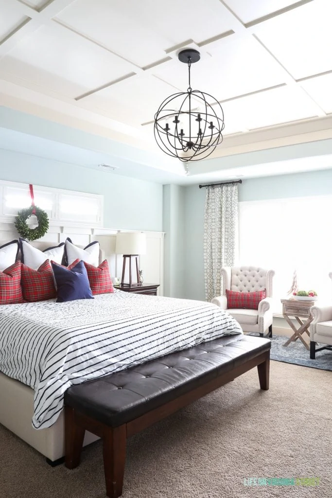 Large bed in middle of room with a chandelier over top of the bed and a bench at the foot of the bed.