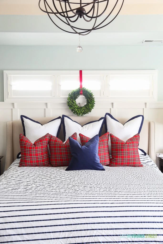 Christmas master bedroom with red plaid pillows, and navy blue and white striped duvet on bed.