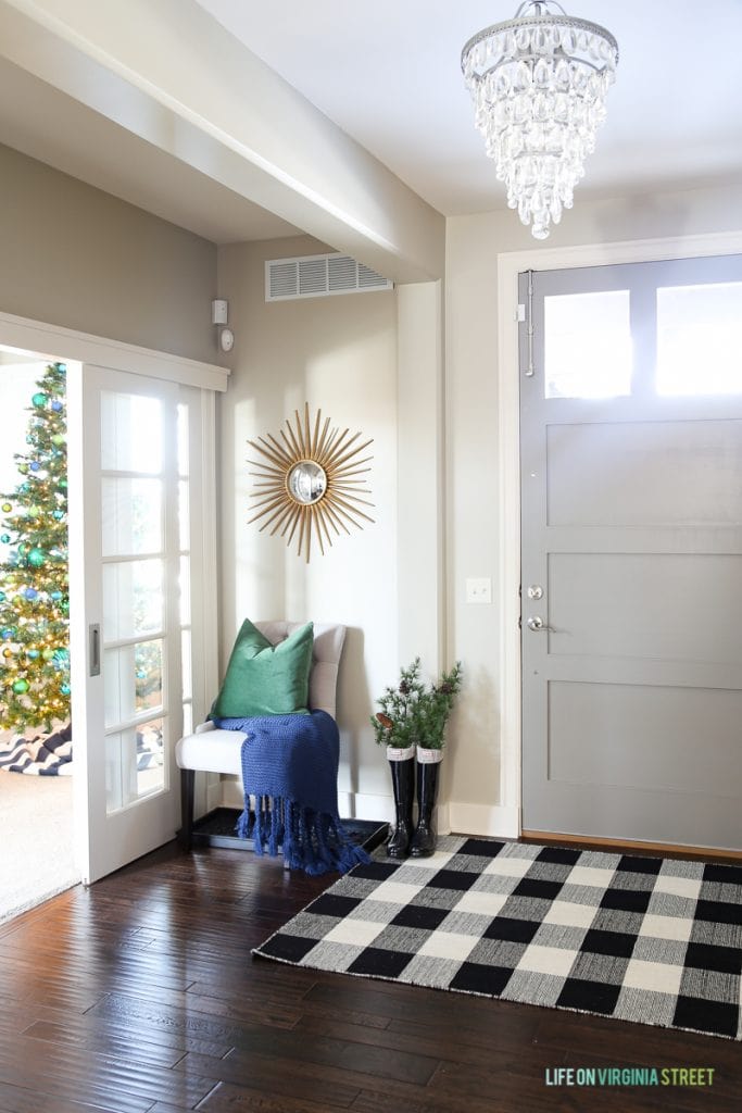 A buffalo checked rug in front of the front door with a chandelier on the ceiling.