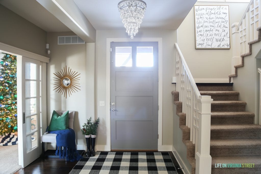 Front door with chandelier in front of it and checked black and white rug on the floor.