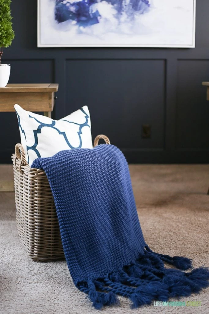 A wicker basket with a navy blue throw and pillow in the basket.