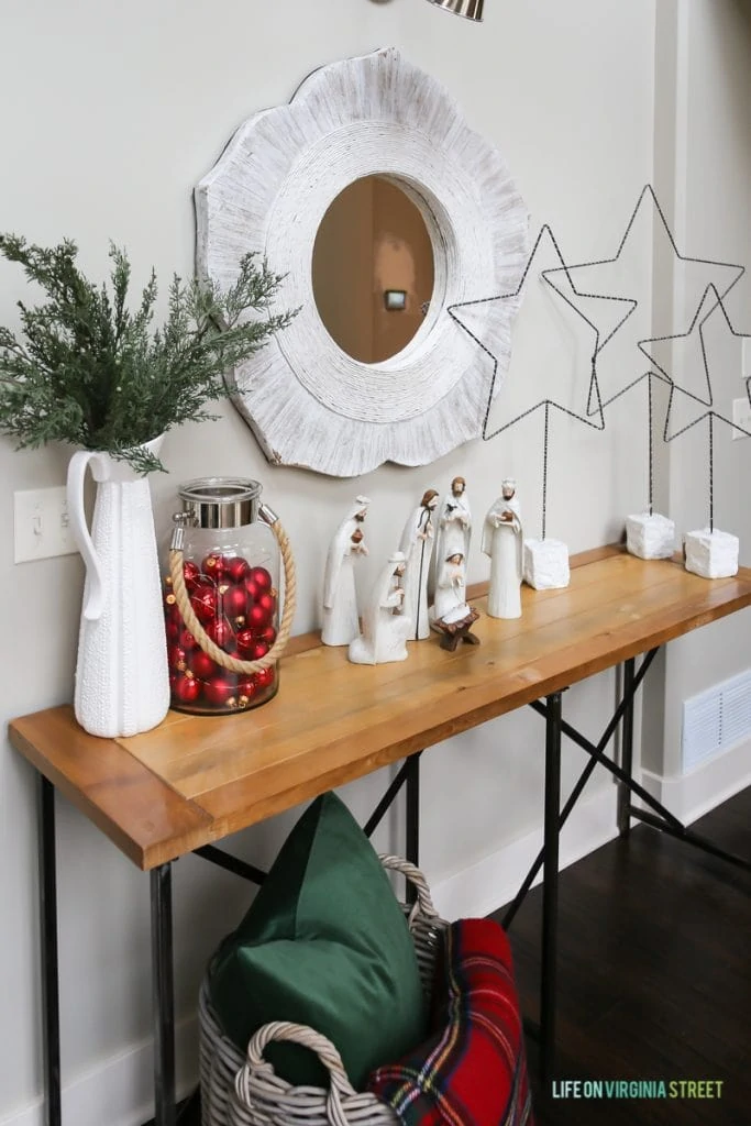 Christmas hallway table with nativity scene, red ornaments in a jar, stars, and a plaid blanket.