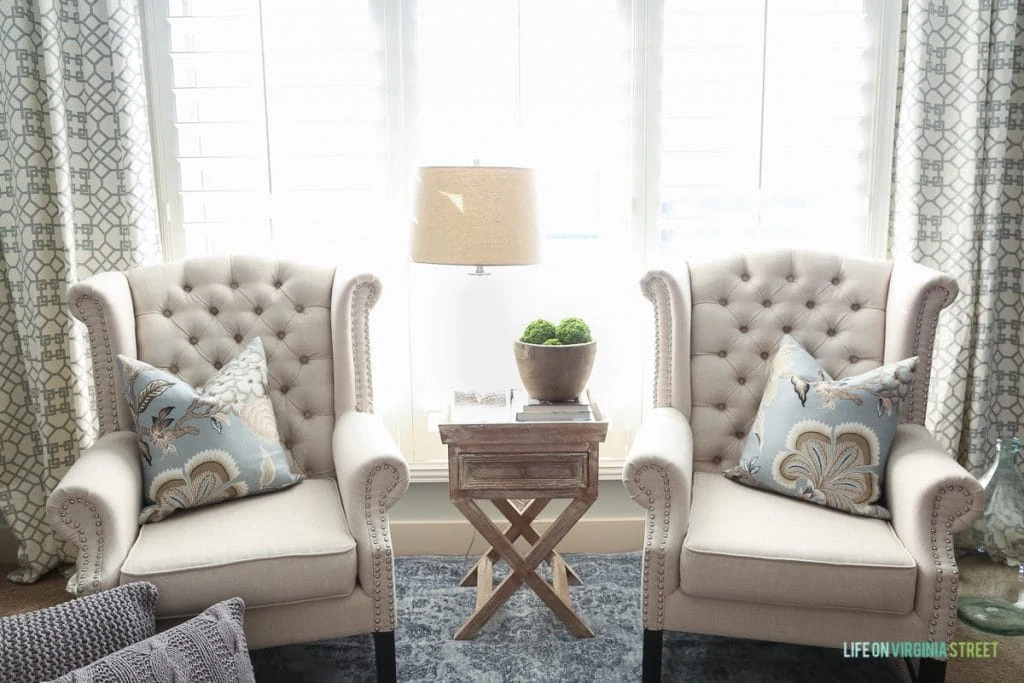 Two neutral colored armchairs in front of window with a side table in between.