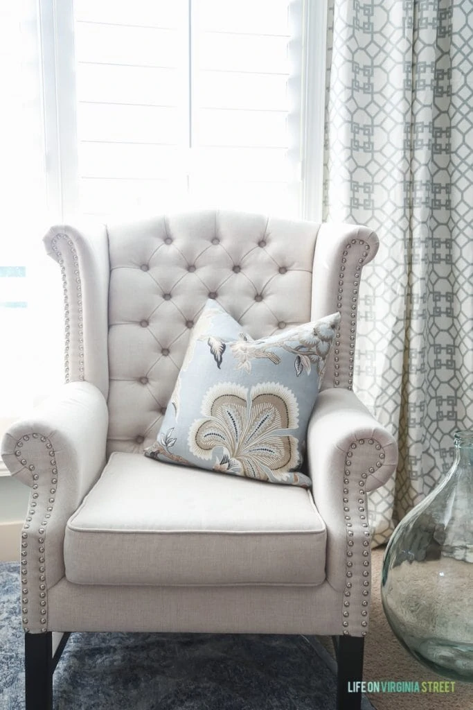 One neutral armchair with light blue, white and beige patterned pillow on the chair.