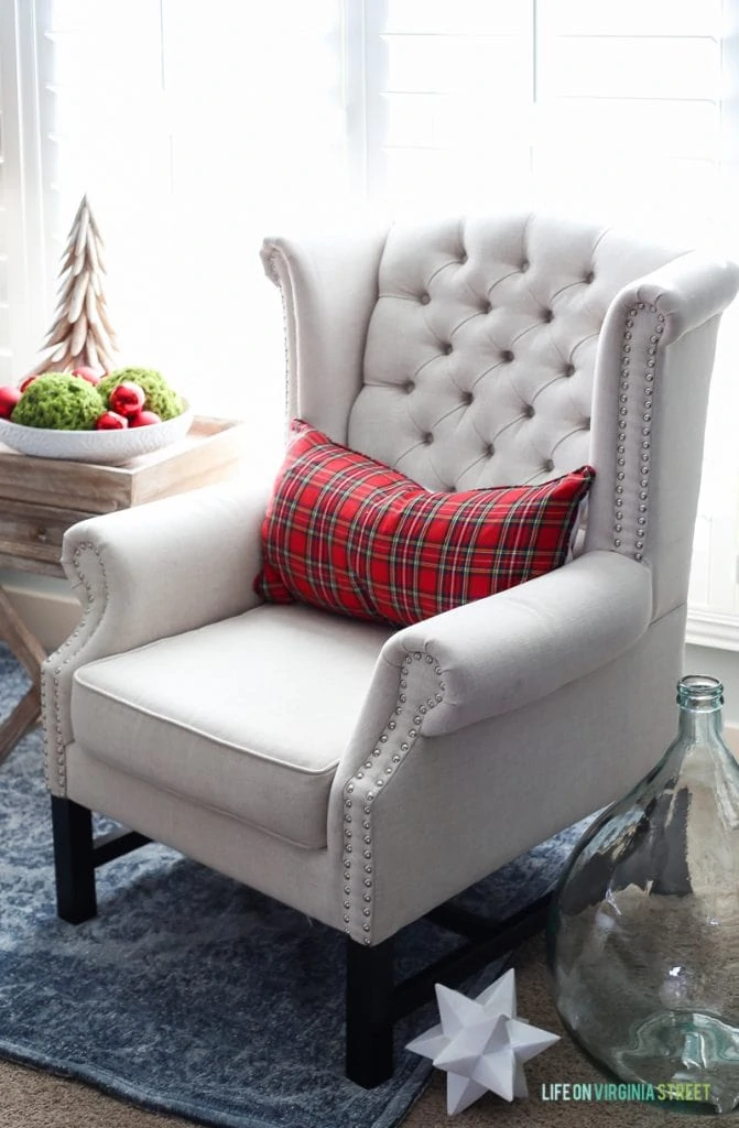 White armchair in bedroom with red plaid pillow on it.