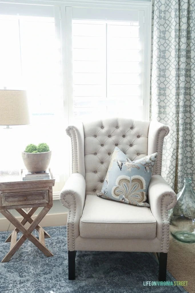 Armchair in corner of room with green and white curtain behind it.