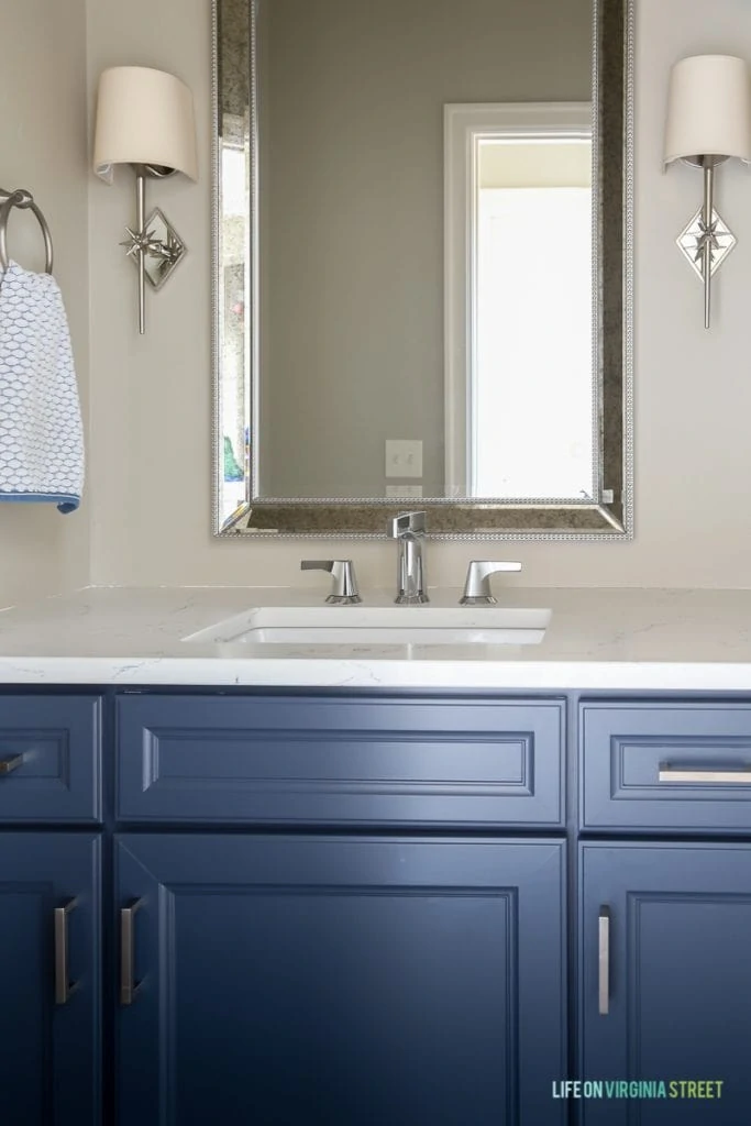 Powder bathroom makeover with freshly painted cabinets and new nautical star sconces, Delta Faucet faucet, Behr Castle Path Walls and Benjamin Moore Hale Navy Cabinets. Love the fresh, nautical vibe! Countertops are Daltile One Quartz in the Luminesce color.