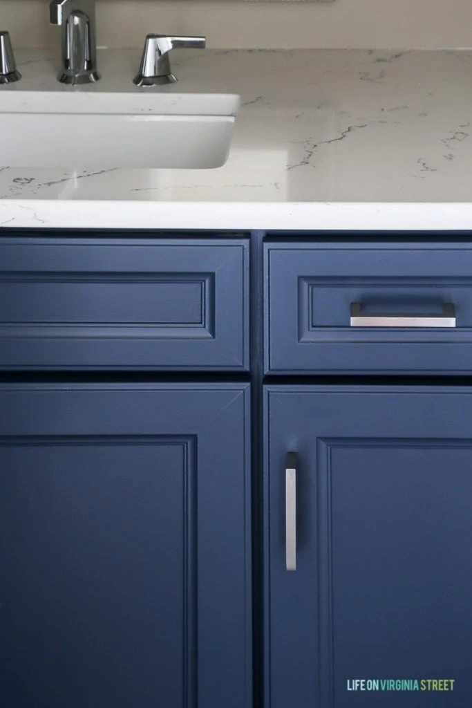 Powder bathroom cabinets freshly painted in a cool navy blue, Delta Faucet faucet, Behr Castle Path Walls and Benjamin Moore Hale Navy Cabinets. Love the fresh, nautical vibe! Countertops are Daltile One Quartz in the Luminesce color.