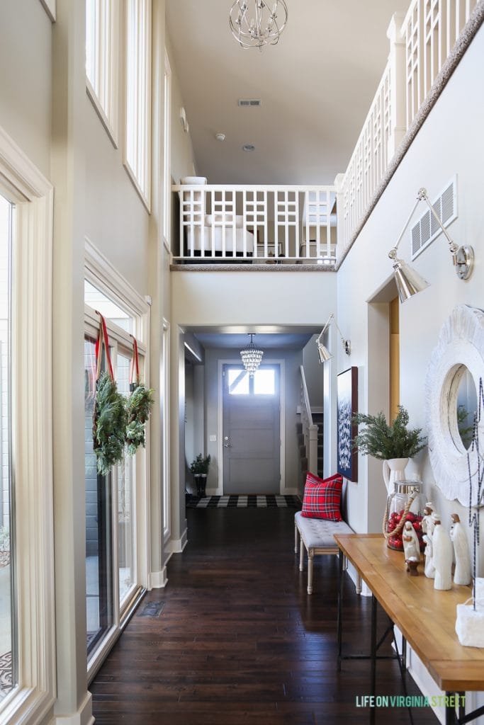 Christmas entryway hallway with linen bench, red plaid pillows, wreaths, swing-arm sconces and 'Doxology' canvas artwork. 