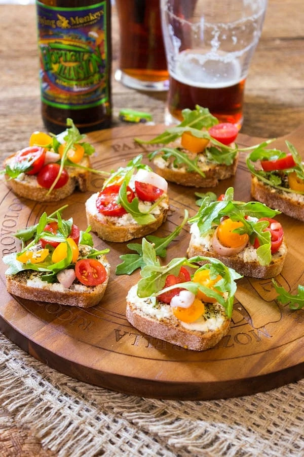 Little toasts with tomatoes and arugula on a wooden tray.