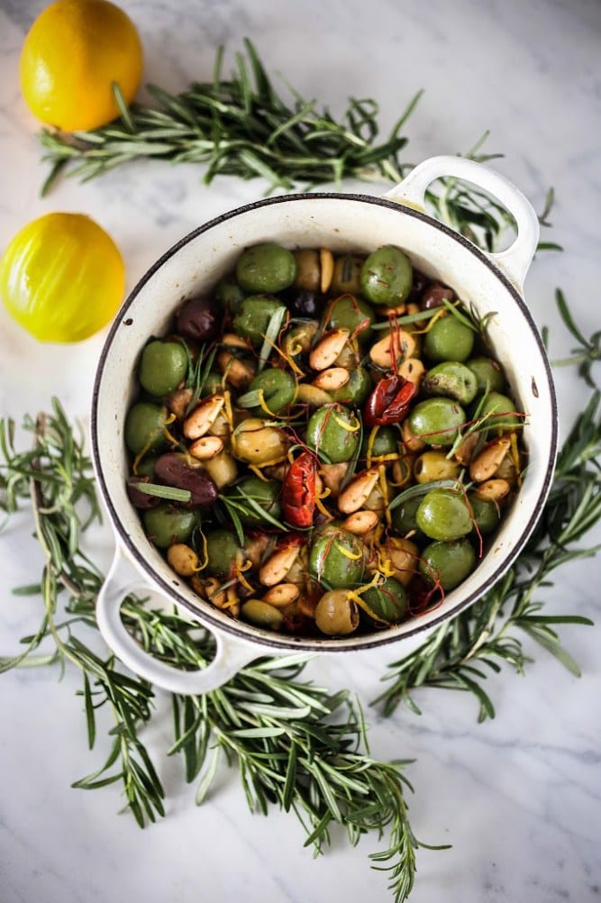 Marinated olives in a white pot with rosemary around it and lemons.